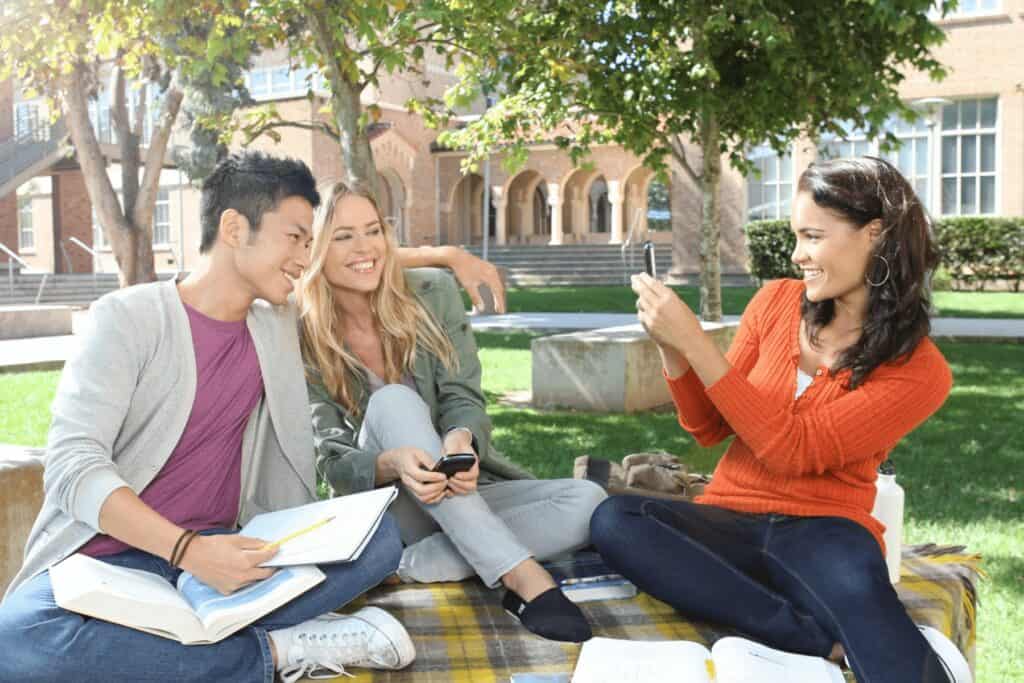 Students taking selfies on the campus lawn.