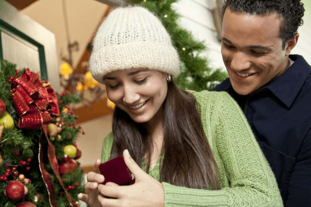 Woman and man looking at engagement ring in room decorated for Christmas.